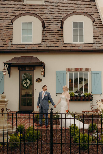 Bride and groom holding hands in front of a cottage