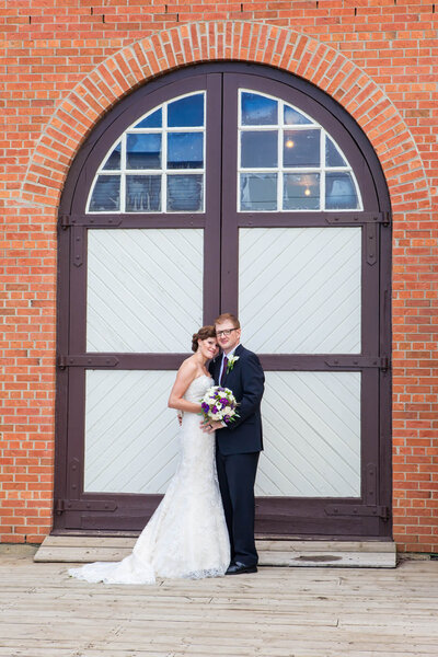 Bride and Groom in front  of rustic firehouse  entrance at Fort Edmonton Park