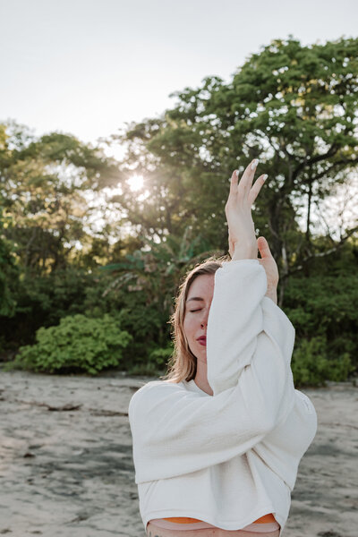 A picture of a woman in a yoga pose on a beautiful beach in costa rica with the beach and jungle in the backdrop