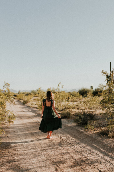 A woman walks down a dirt road in Arizona with cactus