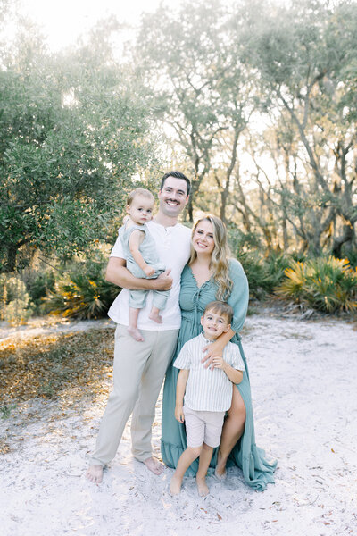 A family of four standing in front of trees looking at the camera during the photography session at sunset in St. Andrews State Park.