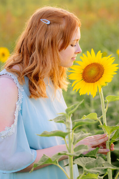 Allie in a sunflower field smelling a sunflower