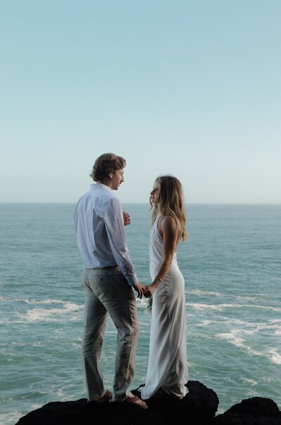 bride and groom standing in front of ocean in kauai