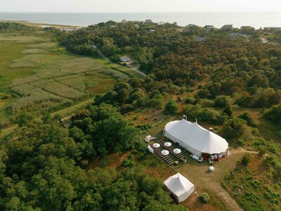 Aerial view of a wedding tent situated in the center of a vast green field on the coast of Cape Cod.