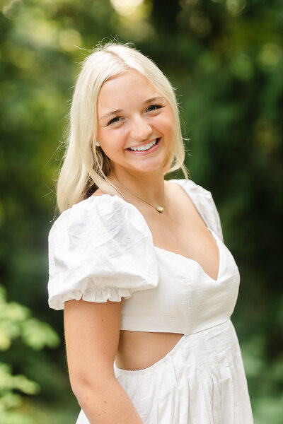 a senior girl wearing a pink shirt leaning against a pole for her senior session