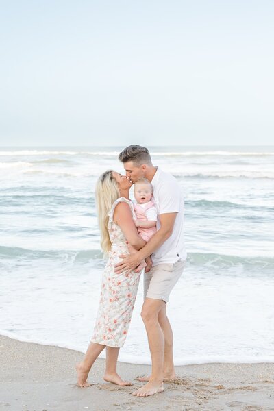 Mom and dad kiss while holding baby