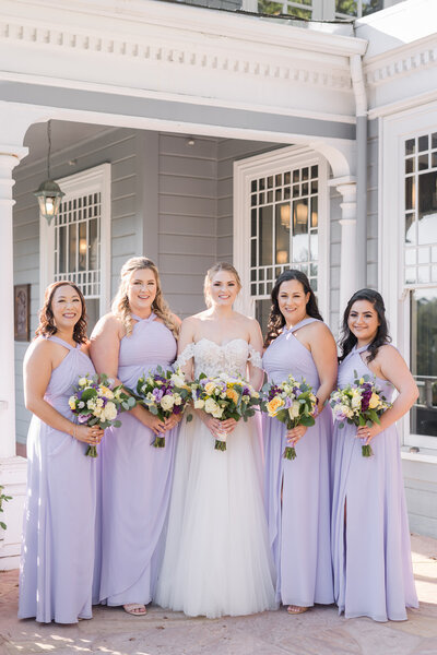 a bride poses with her bridesmaids in purple dresses at a sequoia mansion wedding