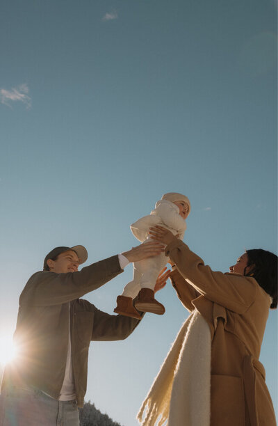 A man handing their baby to his wife in a playful, fun toss.