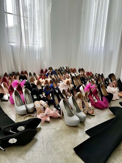 Close up shot of a large collection of shoes and high heels displayed on the floor.