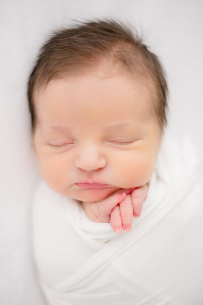 Newborn baby peacefully swaddled in a soft blanket, nestled in a basket surrounded by lush greenery in a garden. The serene setting highlights the baby's calm and gentle presence amidst nature