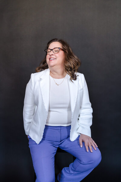 Jen Rigley on stage wearing a white jacket and purple pants.