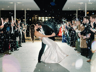 Black and white photo of bride and groom in their getaway car waving and surrounded by bubbles