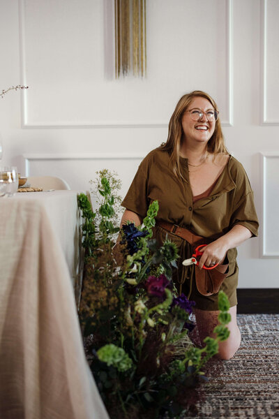Boise, Idaho florist, Hillary Clark, arranges flowers next to a table, representing her vendor profile for the Crush Collective wedding show.