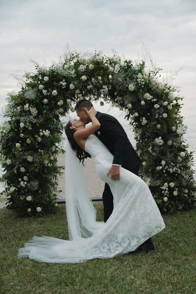Bride and groom sharing a kiss after their wedding ceremony with arched florals in the background