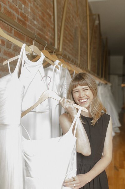Woman holding a wedding dress on a hanger and smiling.