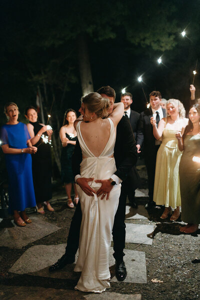 Bride and groom embrace on a dance floor surrounded by guests holding sparklers at night, beautifully captured by a Toronto wedding photographer.