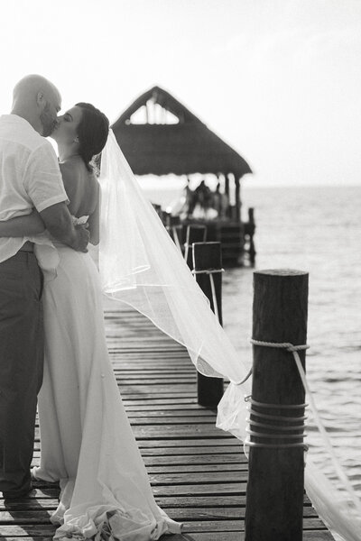 A couple shares an intimate moment on a wooden pier overlooking the ocean at their destination wedding.