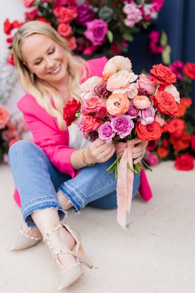 Floral designer holding vibrant bouquet of red, coral, and blush blooms, representing joyful Austin wedding florist style.