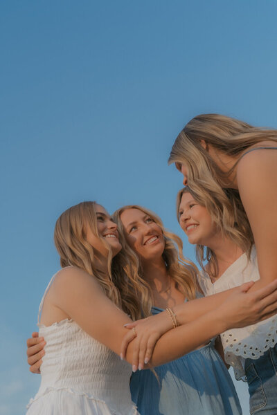 Four senior girls group hug together while they smile at each other. The photographer is on the ground looking up to them and the pretty blue sky is the background in Northeast, TN. 