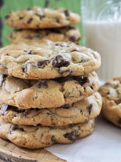 Stack of chocolate chip cookies with a glass of milk in the background.