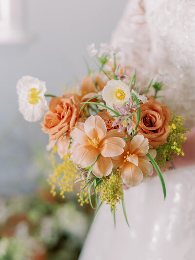 A person holds a bouquet with peach and yellow flowers.