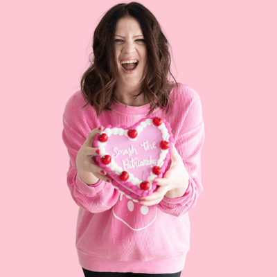 Emily, a brand and web designer, sits at her desk in a pink sweatshirt, speaking into a microphone.