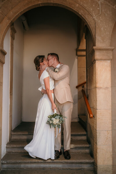 Destination wedding photography of kissing bride and groom on a staircase in a historical building.
