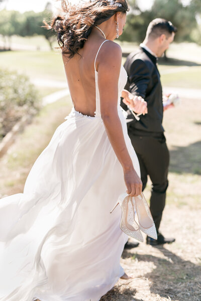 groom escorts bride carrying her wedding shoes
