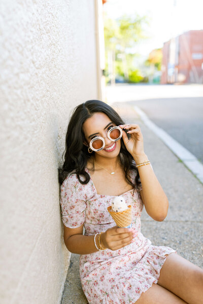 girl with dark hair posing for camera with ice cream cone in hand and glasses in a floral dress