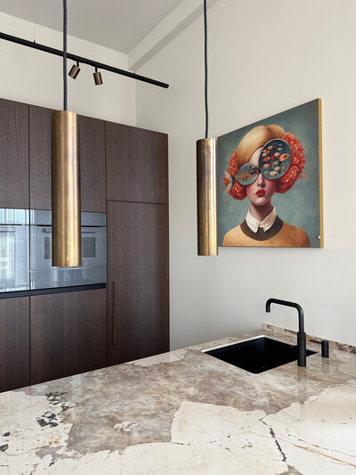 Moderne keuken met marmeren blad, messing hanglampen en kleurrijk portret aan de wand