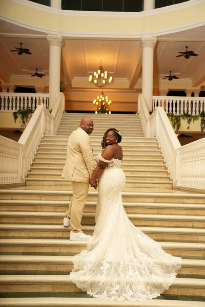 A destination wedding couple poses for a photographer at the Grand Oasis Resort in Jamaica, surrounded by lush tropical scenery.
