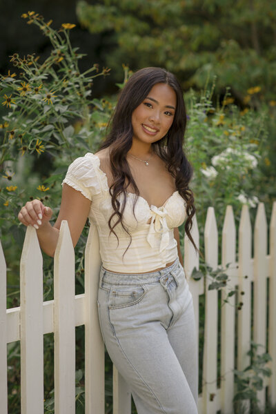 Beautiful senior portrait of a girl standing by a picket fence with florals in the background