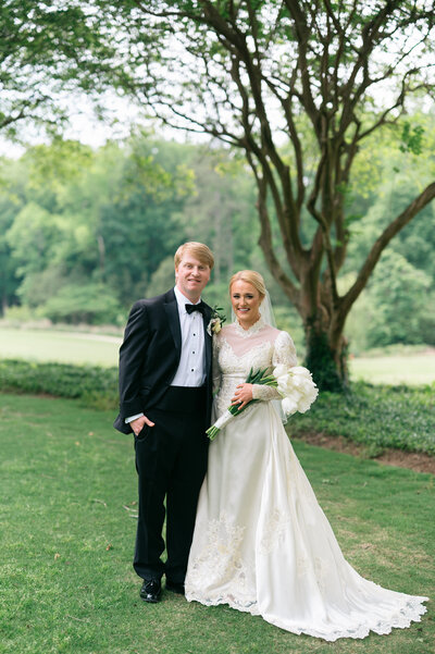 man in black tux standing with woman in white dress that is holding tulips 