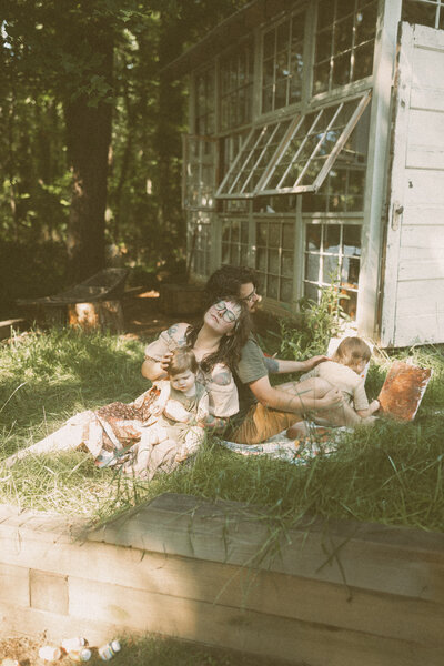 A family of four sits in a sunny spot in the grass at Das Hinterhaus while playing with paints and relaxing. 