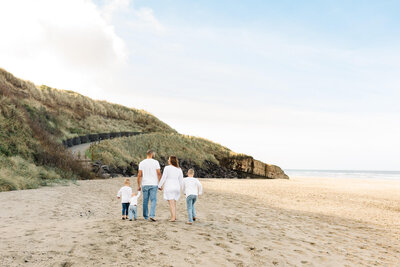 family with young boys dressed in white and denim walking on beach