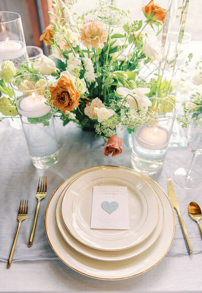 Table setting with gold silverware and an orange, white and green floral centerpiece