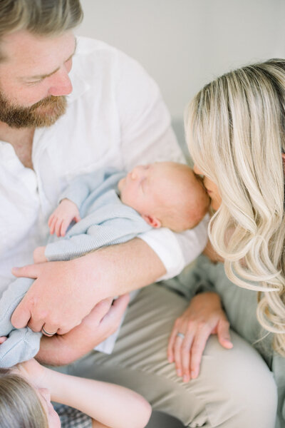 Mom kissing head of baby held by dad in home newborn photography session in home.