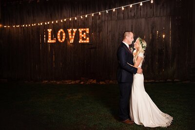 Bride and groom looking at one another during nighttime portraits at the Love sign on the barn of Drakewoood Farm
