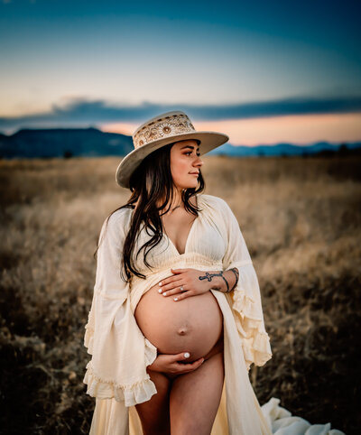Maternity Photographer, an expectant mother holds her belly in dry meadows at dusk