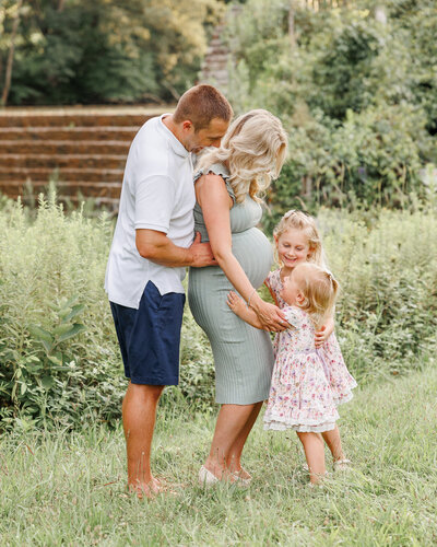 Family with 2 little children embracing mom pregnant with third baby