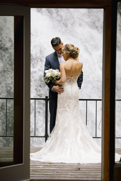 bride and groom stand in front of waterfall at stone tavern farm