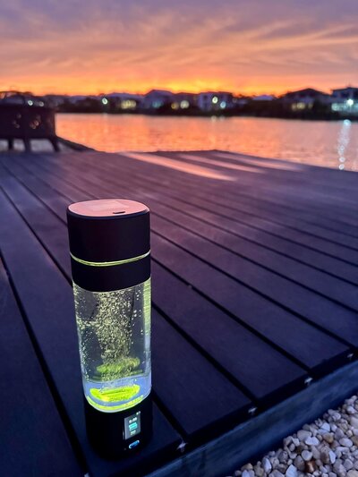 Hydrogen water bottle glowing on a wooden dock at sunset, showcasing a modern hydration resource.