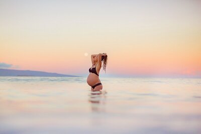 Couple kneeling in the ocean and touching foreheads during babymoon photoshoot on Maui