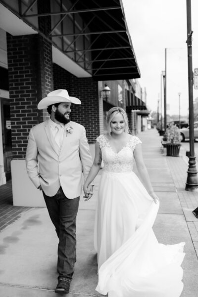 black and white wedding photos with bride and groom holding hands and walking down the  sidewalk as they smile on their wedding day
