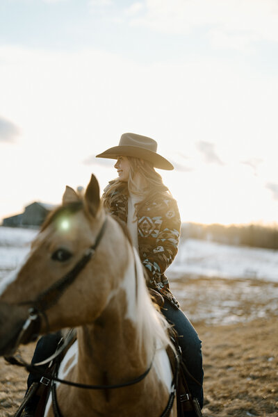 a cowgirl sitting on her horse looking off into the distance during a winter sunset in ontario captured by an equine photographer who specializes in natural light