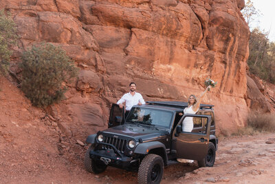 Eloping couple celebrating in a black Jeep at Merry Go Round Rock in Sedona, Arizona, with the bride holding her bouquet triumphantly against a backdrop of rugged red rock cliffs.