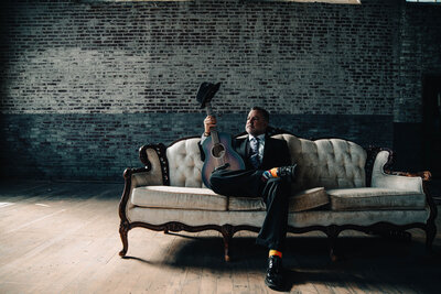 A person sitting on the couch with a guitar and a hat on top 
