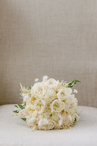 A glamorous bridal bouquet with lush white flowers rests on a beige chair.