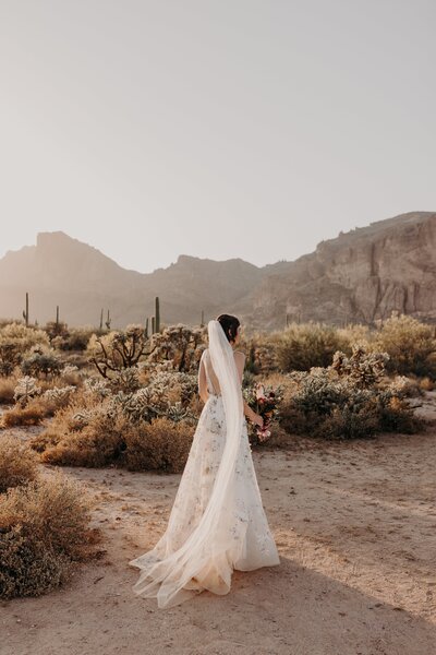 Bride walks away from camera with veil flowing in the wind holding bouquet