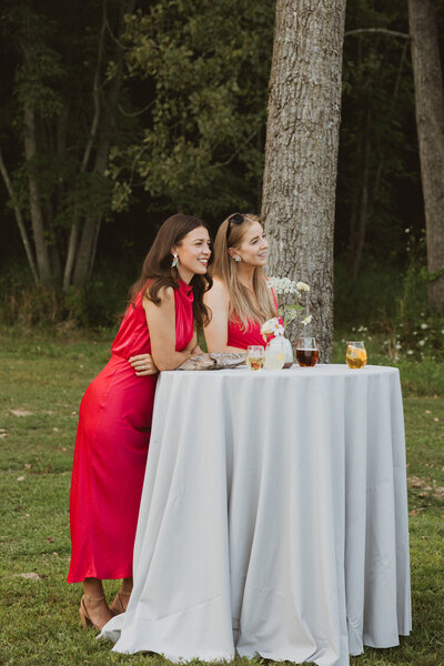 Two women in red dresses standing at a cocktail table